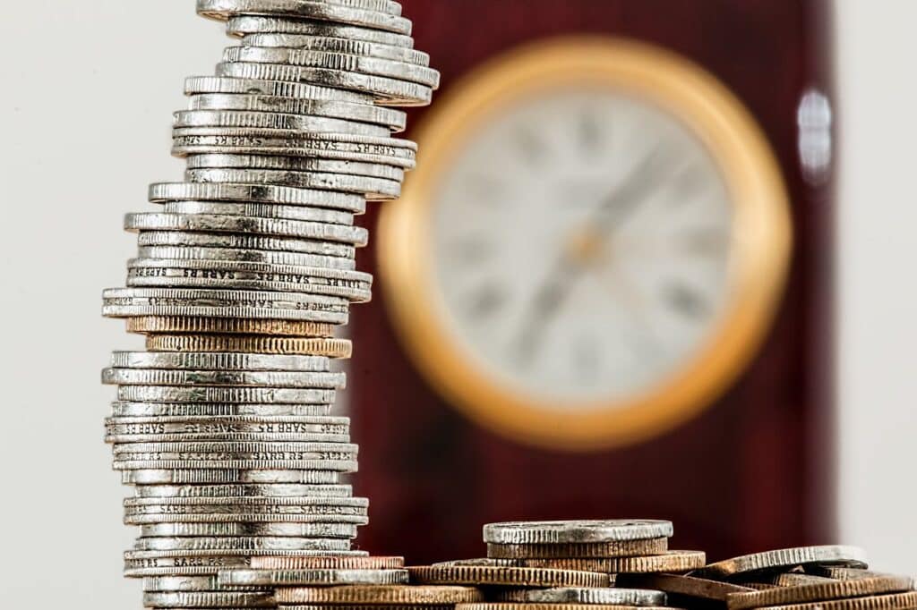 Stacks of coins in front of a clock, showing savings growing over time.