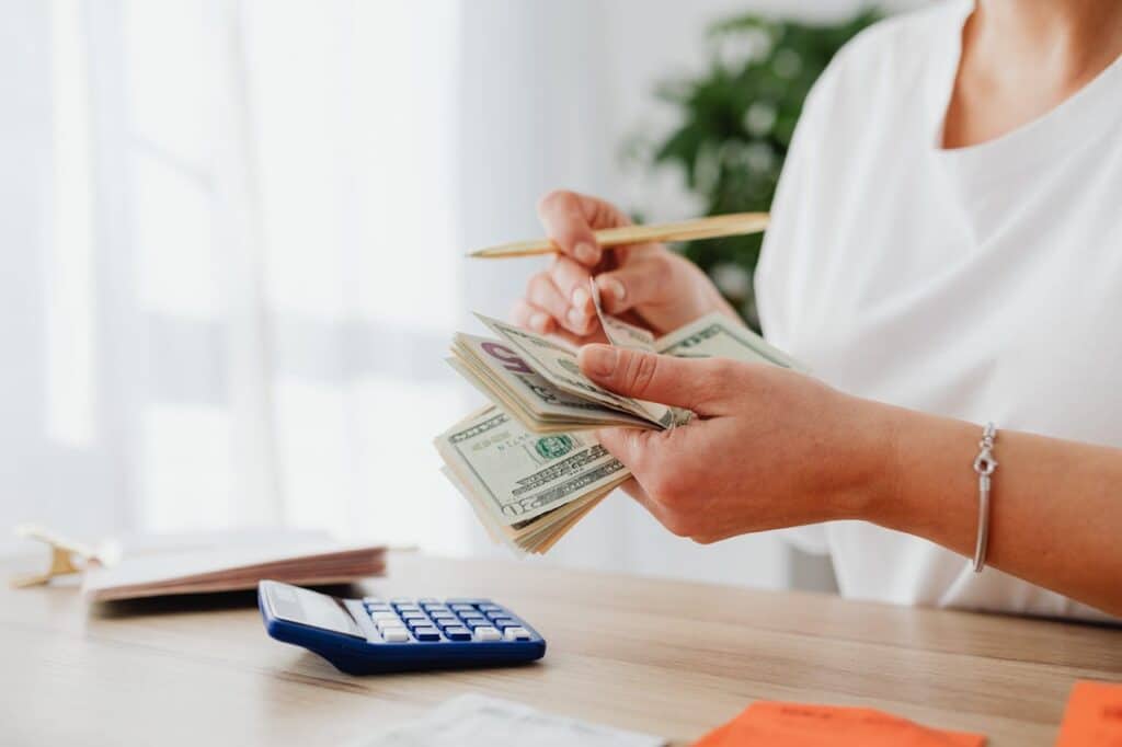 Counting dollar bills with a calculator to set a small-paycheck budget.