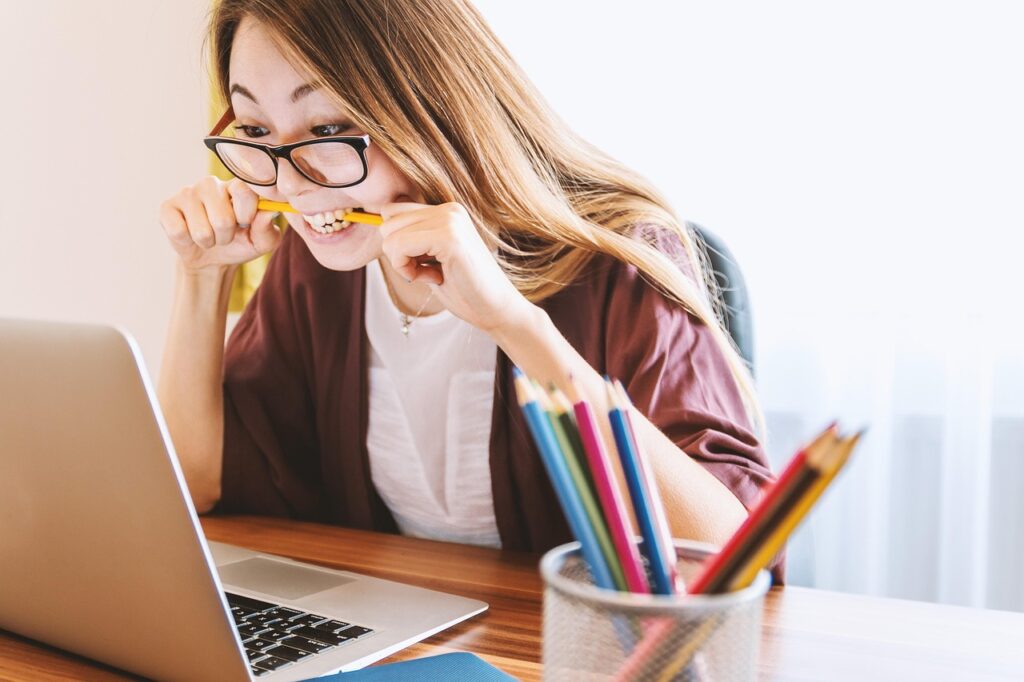 woman biting pencil while looking at laptop due to money anxiety