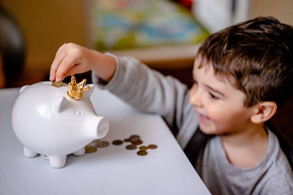 Child putting a coin into a piggy bank, starting an emergency fund with small amounts.